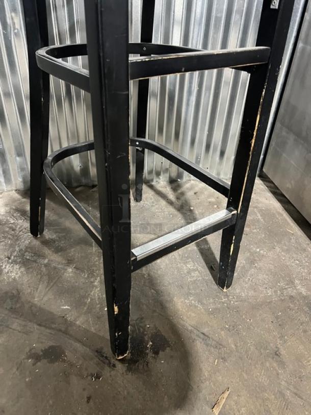 Commercial black bar-height chair, metal frame, visible wear, sturdy construction, ideal for bar settings.