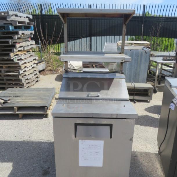 True TSSU-27-06-HC refrigerated prep table with 2 stainless steel shelves and 24" ticket rail, on casters. 27.5"x31.5"x67".