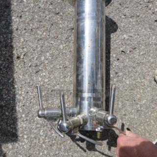 Stainless steel wine tower with three taps, polished finish, outdoor setting, shows minor wear, ideal for home bars.