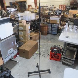 Metal display rack on casters, adjustable height, sturdy black frame, multiple wire arms for hanging items, used condition.