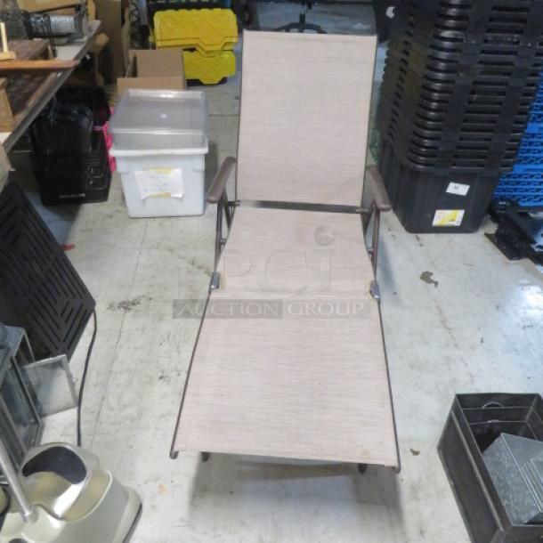 Foldable lounge chair, light brown fabric, metal frame, condition appears used, suitable for outdoor or patio use.