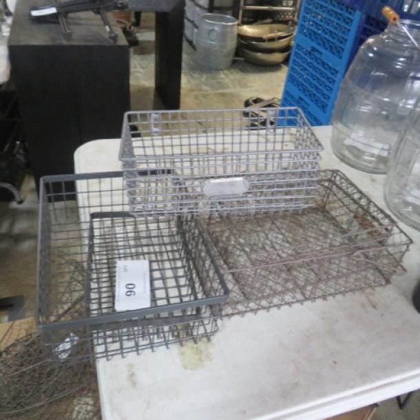 Assorted wire baskets in varying sizes, gray and metal tones, some with visible auction tags, displayed on a table.
