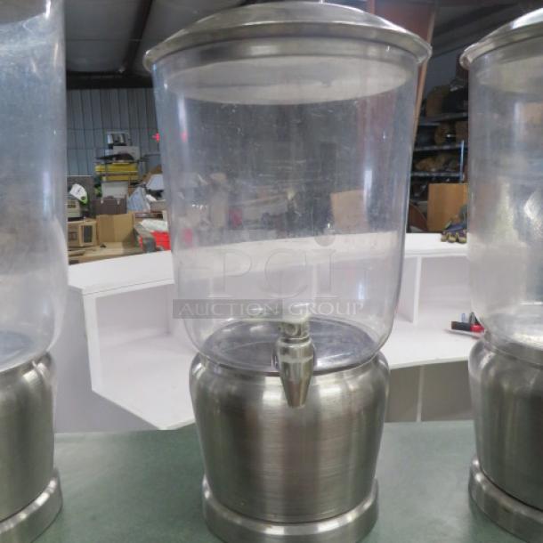 Stainless steel and poly beverage dispenser, clear body with metal base and spout, used condition, no visible markings.