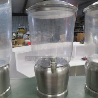 Stainless steel and poly beverage dispenser, clear body with metal base and spout, used condition, no visible markings.