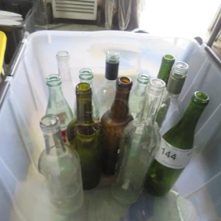 Assorted glass bottles in a plastic bin, various colors and sizes, one bottle marked with tag "144." Mixed vintage collection.
