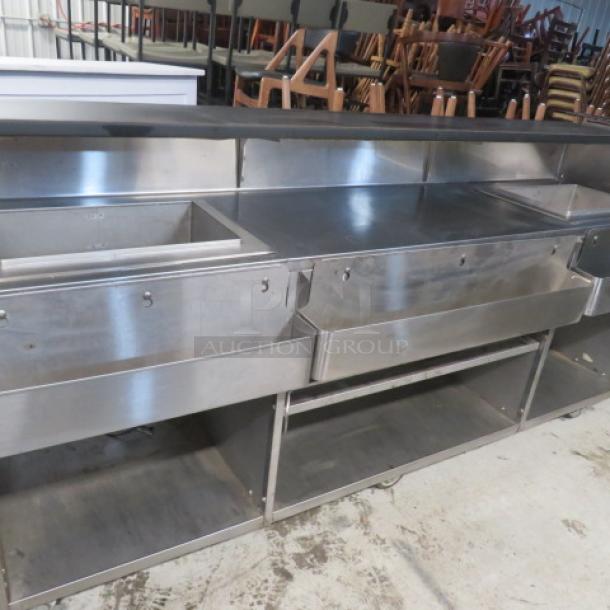 Portable bar with two stainless steel ice wells, two 26.5" bottle rails, and one 39.5" bottle rail under storage. Black laminate serving shelf on casters, dimensions 95x31x46.