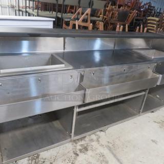 Portable bar with 2 stainless steel ice wells, 2 bottle rails, 39.5-inch bottle rail under storage, black laminate shelf, on casters.