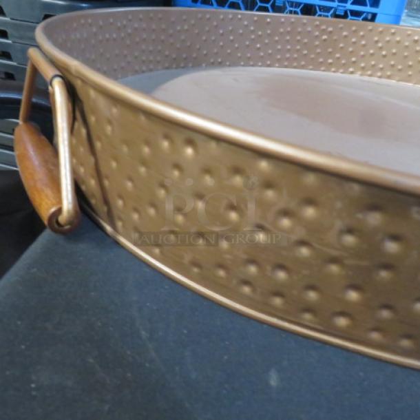 Copper-colored hammered round serving tray, 16.5x2.5 inches, with wooden handles. In good condition.