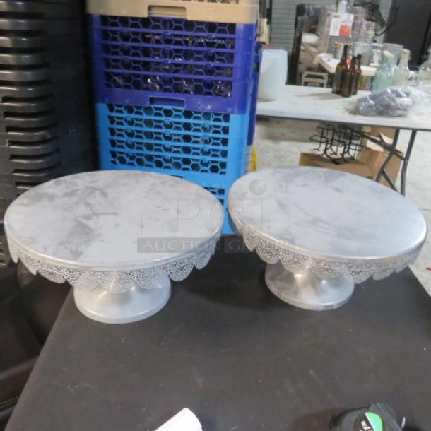 Two 12-inch cake stands with lace-like edge details, made of silver-tone metal. Slightly used condition.