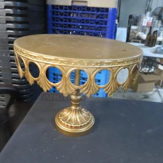 Gold-toned 12-inch cake stand with ornate cutout design, featuring a round top and decorative pedestal base, in good condition.