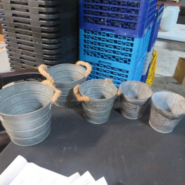 Assorted galvanized buckets, various sizes, with rope handles and embossed labels, showing light wear.