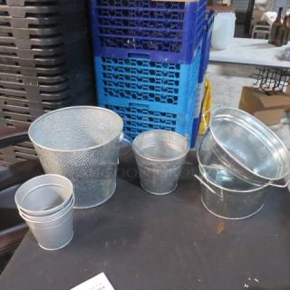 Assorted metal buckets in various sizes on a table, including textured and galvanized types. Good condition. Model 7XBID.
