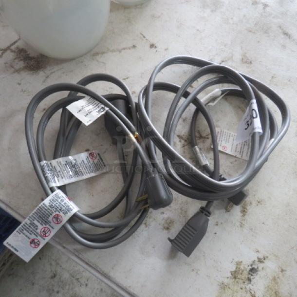 Gray electrical cords, 250 Volt, 9A, 20AMP, with attached warning labels and two-prong plugs, coiled on a tabletop.