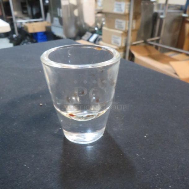 Clear glass shot glass, 10XBID model, in good condition with slight surface marks, displayed on a dark surface.