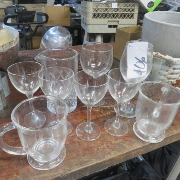 Assorted lot of drinking glasses, including wine glasses, mugs, and tumblers on a wooden table. Various styles and conditions.