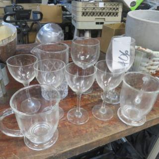 Assorted lot of drinking glasses, including wine glasses, mugs, and tumblers on a wooden table. Various styles and conditions.