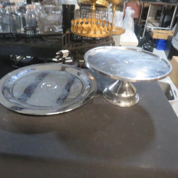 Assorted stainless steel display stands; includes one flat and one elevated stand. Shiny finish, good condition.