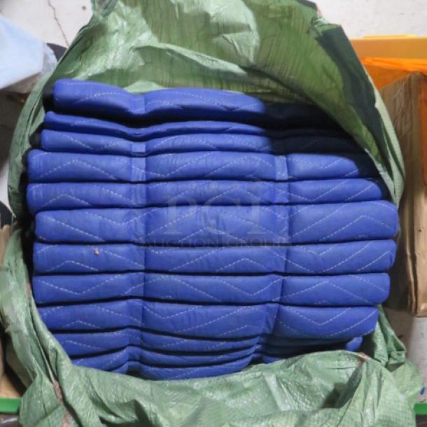 A bundle of blue moving blankets, new and folded, in a green bag. Quilted design, durable fabric. Ideal for moving protection.