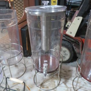 Clear beverage dispenser with metal stand and lid, featuring a spigot for easy pouring. Well-maintained condition.