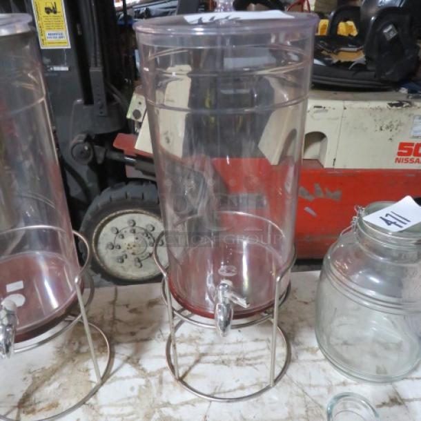 Clear cylindrical beverage dispenser with metal stand and spigot. Good condition, ideal for events or gatherings.