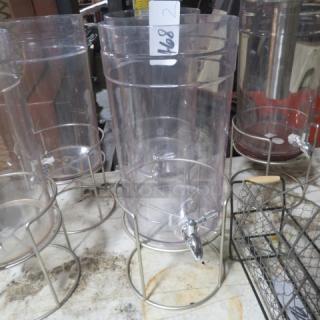 Clear plastic beverage dispenser with metal stand, missing lid. Appears in used condition. Tag reads "168 2".
