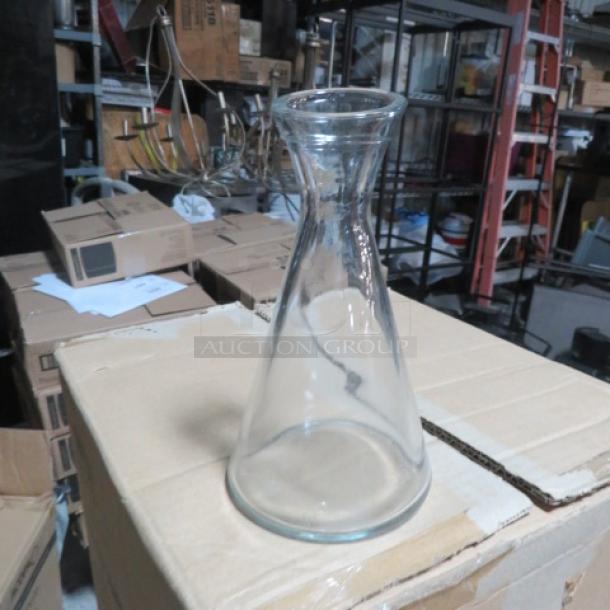 Clear glass carafe with wide base, narrow neck, excellent condition, Item 6XBID, displayed in warehouse setting.