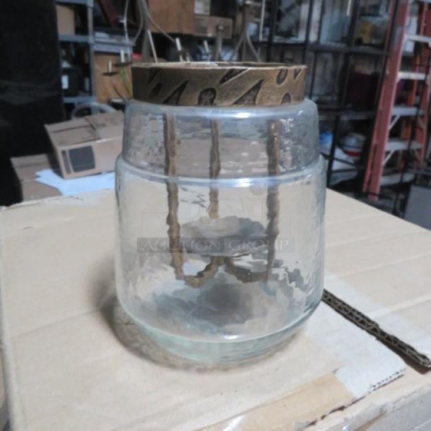 Glass candle holder with a decorative metal top, featuring a rustic design. Used condition. Model: 5XBID.