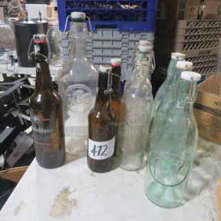 Lot of assorted hinged lid bottles, various sizes, some with embossed designs. Includes branded and numbered bottles. Used condition.