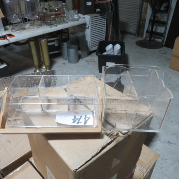 Assorted acrylic organizers with multiple compartments, clear, in good condition, placed on cardboard boxes in a warehouse setting.