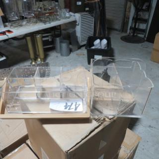 Assorted acrylic organizers with multiple compartments, clear, in good condition, placed on cardboard boxes in a warehouse setting.