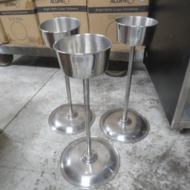 Three stainless steel champagne/wine bottle holders with pedestal bases. Sturdy and polished, suitable for elegant displays.