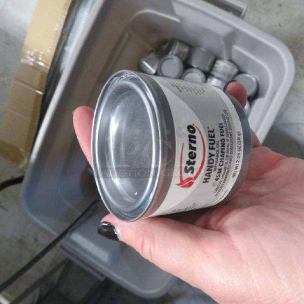 Hand holding a can of Sterno Handy Fuel. Features visible label with brand name and description. Other cans in a plastic bin.