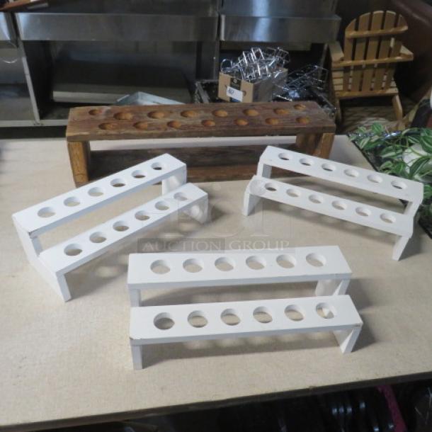 Assorted wooden shot holders in various styles, including four white stands and one rustic brown holder, each with multiple slots.