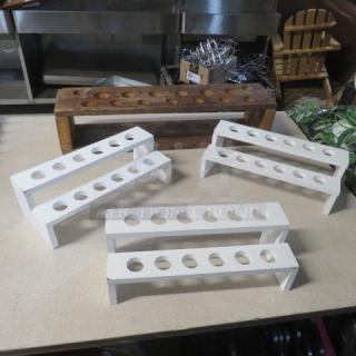 Assorted wooden shot holders in various styles, including four white stands and one rustic brown holder, each with multiple slots.