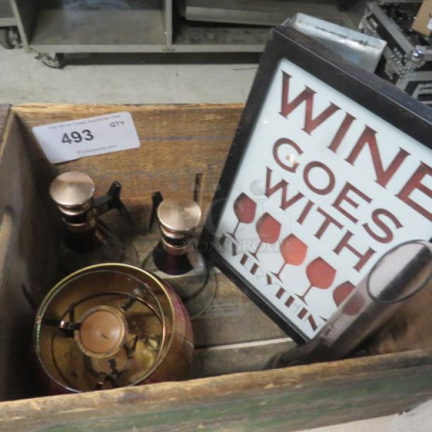 Wooden box containing assorted decor items, including a framed "Wine Goes With" sign and decorative bottles. Condition appears good.