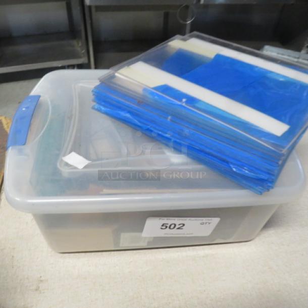 Clear plastic storage bin containing assorted items, with a label marked "502 QTY." Stacked blue file folders on top.