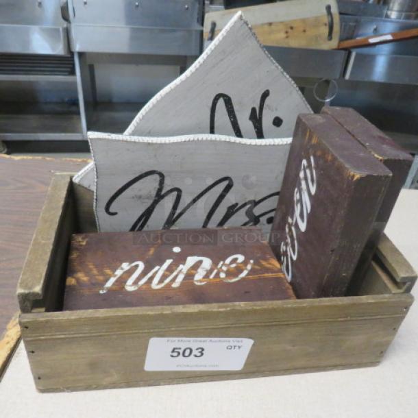 Wooden crate containing rustic signs, including "Mr." and "Mrs." and number "nine." Signs show wear, aesthetic vintage style.