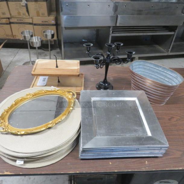 Assorted home décor lot featuring a gold-framed mirror, metal trays, candle holder set, and woven placemats.