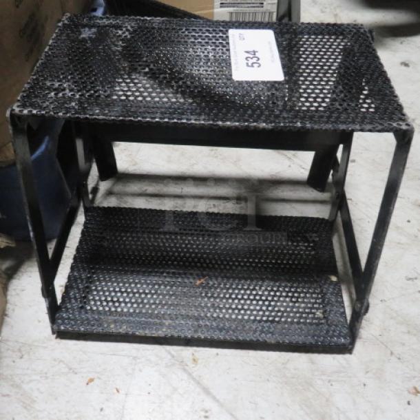 Black metal 2-tier display stand with perforated shelves, used condition. Tags show "534." Ideal for retail or home use.