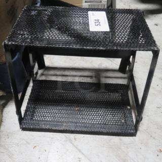 Black metal 2-tier display stand with perforated shelves, used condition. Tags show "534." Ideal for retail or home use.