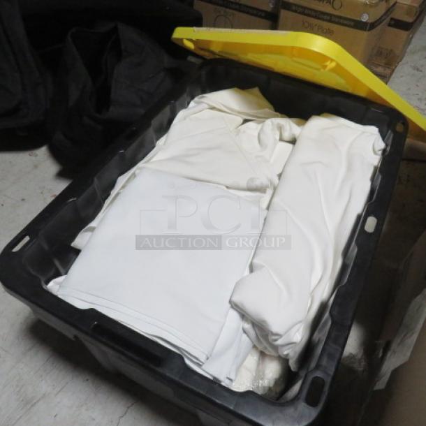 A stack of white linens in a black storage bin. Linens appear neatly folded and clean, suggesting good condition.