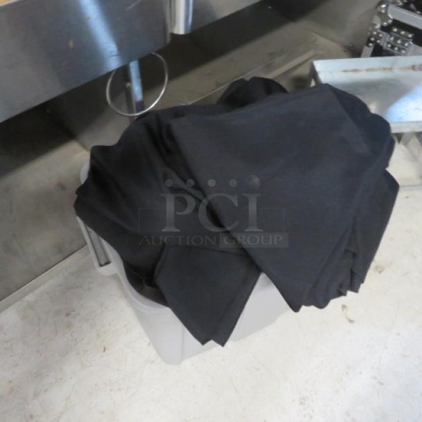 A bin filled with black assorted linens in good condition, placed on a white floor near metal equipment.