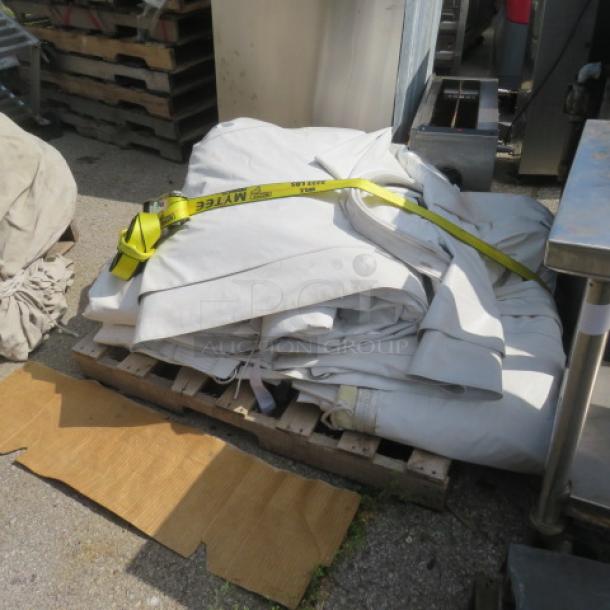 White event tent fabric folded on a pallet, secured with a yellow strap. Outdoor setting, used condition. No visible markings.