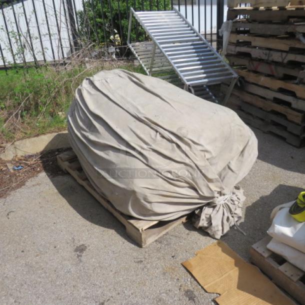 Wrapped event tent on a wooden pallet, outdoors. Fabric is beige and weathered, suggesting prior use.