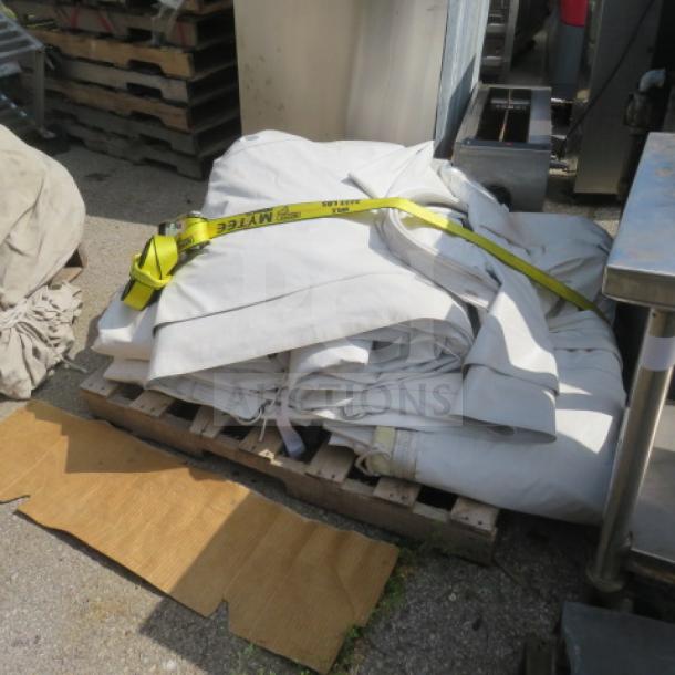 Commercial semi-permanent event tent, folded and secured with a yellow strap, on a pallet, appears lightly used.