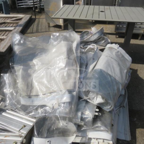 Bundle of components for a commercial semi-permanent event tent, including metal frames and transparent tarps, in used condition.