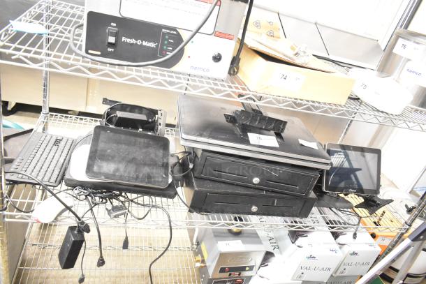 Alt Text: 
Auction items on a wire shelf, including two black cash drawers and five POS monitors. Tags visible with item numbers.