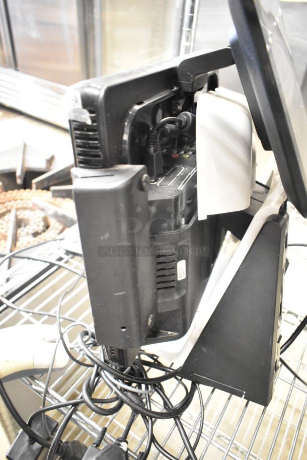 10 POS monitors and accessories, including cables and cash drawers, stacked on shelving. Used condition.