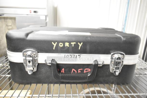 Black Rae hard case with metal latches, handle, and markings "YORTY" and "103215" on a metal shelf.