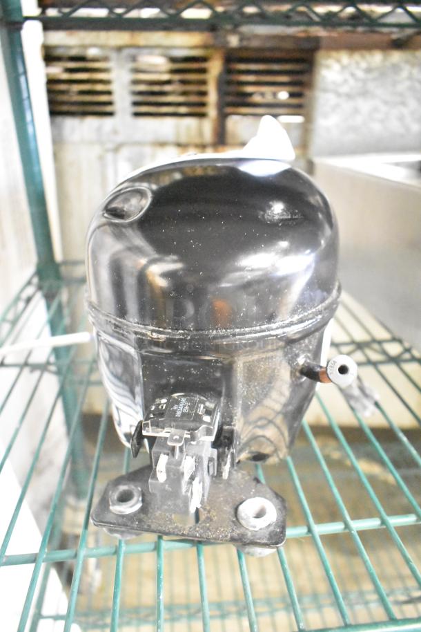 Cubigel NUT55NR Compressor, 151-127 Volts, 1 Phase, black finish, intact condition, mounted on a metal shelf.